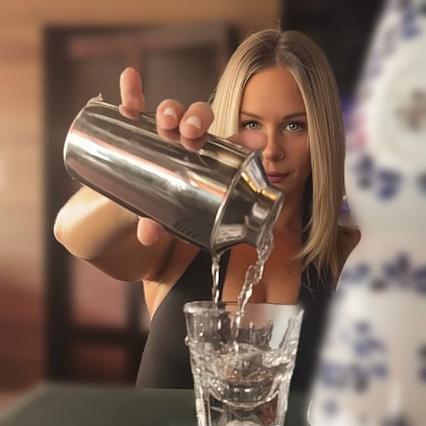 A blonde bartender at Kelly Brothers Irish Pub pours a drink from a shaker into a glass.